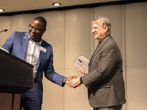 Fred Whitt and Harry Titus shake hands by the podium on the PE Monroe stage